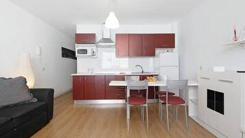 A modern kitchen with white cabinets, a dining table with chairs, a black sofa, and a pendant light.