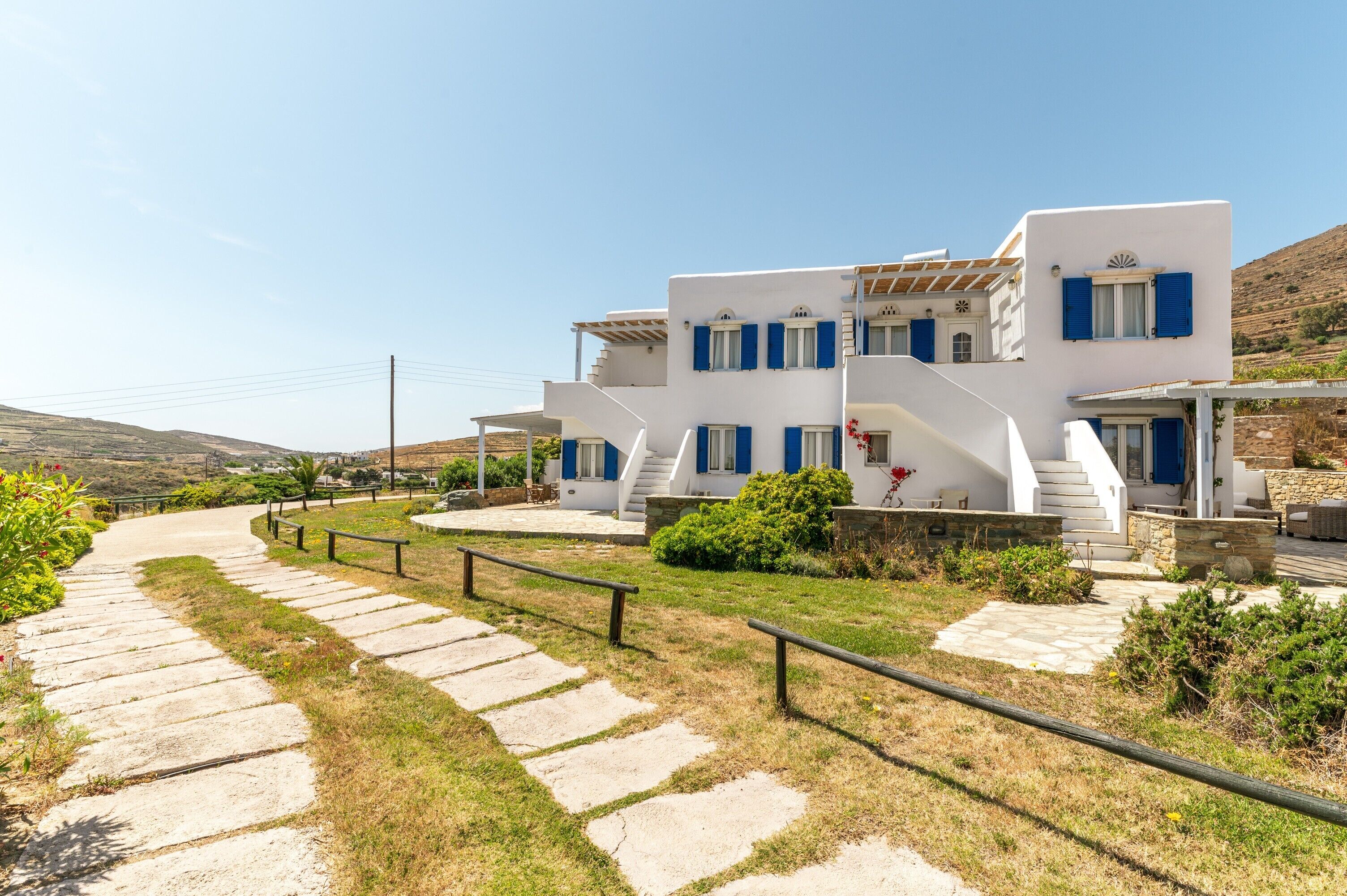 A white building with blue shutters, a stone pathway, and a clear sky.