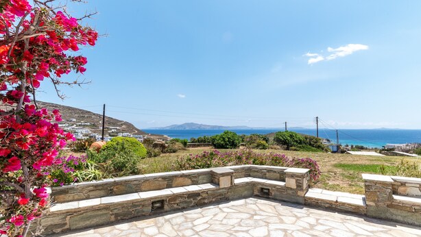 A stone patio with steps leading to a seating area, overlooking a coastal landscape with a view of the sea and distant hills. - Holiday Home 'Anemologio 101 Tinos' with Sea View, Wi-Fi and Air Conditioning (Laouti)