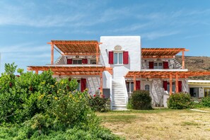 Un bâtiment blanc avec des volets rouges et une pergola en bois, entouré de verdure.
