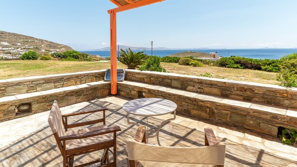 Un patio al aire libre con paredes de piedra, una pérgola de madera y vistas al mar.