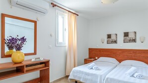 A hotel room with two beds, a wooden desk, a mirror, and a window with curtains. - Holiday Home 'Anemologio 204 Tinos' with Sea View, Wi-Fi and Air Conditioning (Laouti)