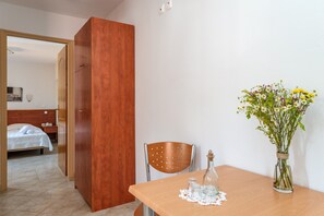 Una habitación con un armario de madera, una mesa de comedor de madera con un florero y una silla, y una cama al fondo.