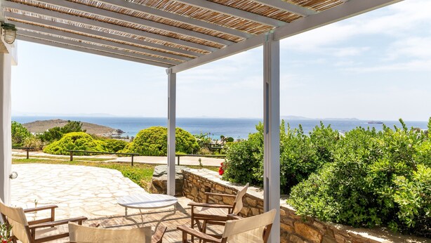 Un espacio al aire libre cubierto con suelo de piedra, mobiliario de madera y vistas al mar.