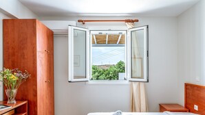 Un dormitorio con una cama, un armario de madera, una mesita de noche y una ventana con un persiano abierto.