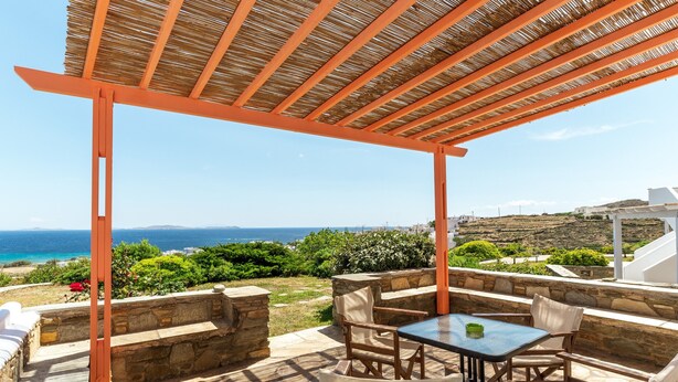 A covered outdoor seating area with stone walls and a view of the sea.