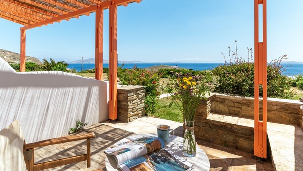 Un espace extérieur abrité, aménagé avec des sièges, offrant une vue sur la mer, des murs en pierre et un vase rempli de fleurs.