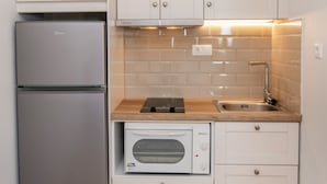 Une cuisine de taille réduite, avec des meubles blancs, un réfrigérateur en acier inoxydable, un four à micro-ondes et un évier.