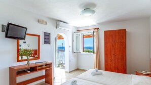 Une chambre d’hôtel avec un lit, une télévision, un bureau, une armoire et une vue sur la mer.