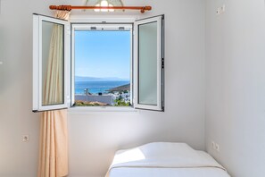 Une chambre à coucher avec un lit, une fenêtre avec des rideaux et une vue sur la mer et les bâtiments.
