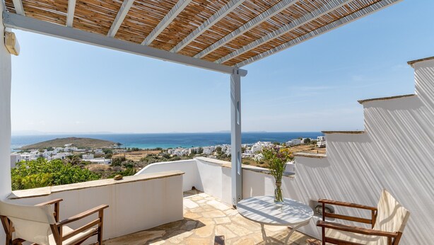 A covered outdoor seating area with a view of the sea and buildings.