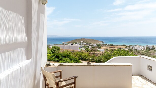Un balcone con vista sul mare, pareti bianche e una sedia.