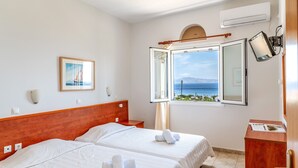Camera d'albergo con due letti, una finestra vista, un quadro appeso e una scrivania con un giornale.