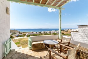 A terrace with a table and chairs, overlooking a coastal town with white buildings and a clear sky.