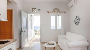 A white room with a white sofa, a small table, and a view of the sea through a window. - Holiday Home 'Anemologio 102 Tinos' with Sea View, Wi-Fi and Air Conditioning (Laouti)