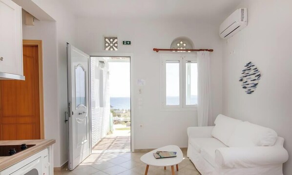A white room with a white sofa, a small table, and a view of the sea through a window.