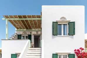 A white building with green shutters, a wooden pergola, and a staircase leading to an entrance.