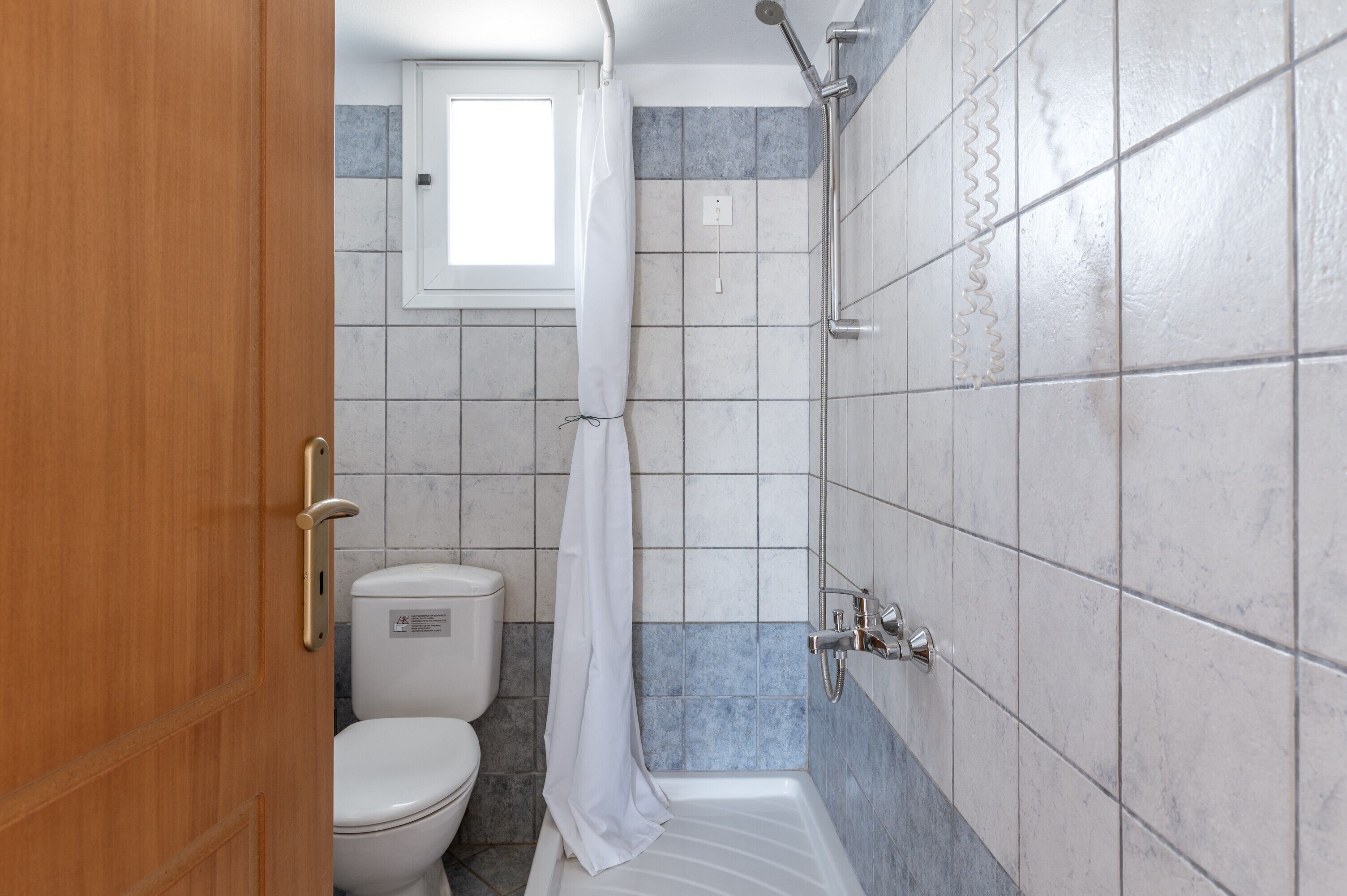 A bathroom with a toilet, shower, and a window.