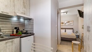 A modern kitchen with a built-in oven, a small refrigerator, and a sink. There is a dining area with a table and chairs, and a bedroom with a bed and a nightstand. - Studio Apartment 'Mella Roa Amar' with Shared Terrace, Wi-Fi and Air Conditioning (Lefkada)