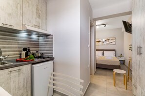 A modern kitchen with a built-in oven, a small refrigerator, and a sink. There is a dining area with a table and chairs, and a bedroom with a bed and a nightstand. - Studio Apartment 'Mella Roa Amar' with Shared Terrace, Wi-Fi and Air Conditioning (Lefkada)