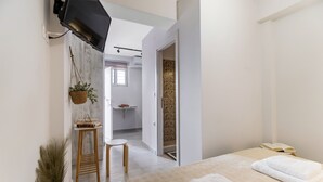 A modern hotel room with a bed, a television mounted on the wall, a small stool, a hanging plant, and a view into the bathroom. - Studio Apartment 'Mella Roa Amar' with Shared Terrace, Wi-Fi and Air Conditioning (Lefkada)