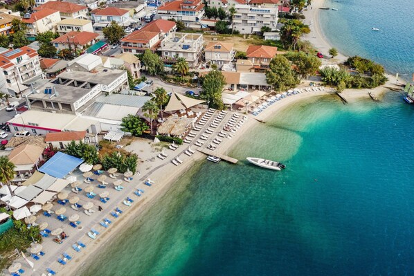 An aerial view of a coastal town with a beach, a marina, and several buildings with balconies.