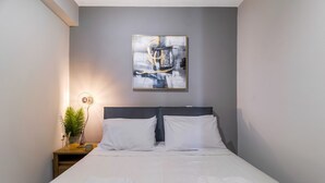 A neatly made bed with white linens and towels, a bedside table with a lamp, and a wall-mounted abstract painting. - Studio Apartment 'Mella Roa Teal' with Shared Terrace, Wi-Fi and Air Conditioning (Lefkada)