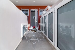 Een balkon met een witte metalen tafel en stoelen, een rode bloem en een schuifdeur met glas.