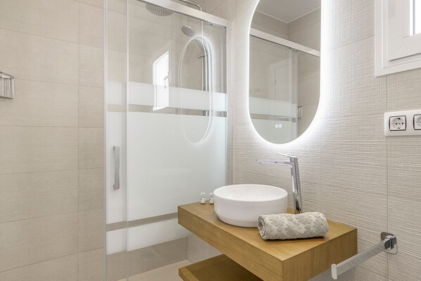 A modern bathroom with a glass-enclosed shower, a round sink, and a wooden vanity.