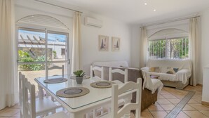 A bright room with a glass table, white chairs, a sofa, and a view of greenery outside. - Holiday Home 'Chalet Fuente2 Shared Pool Family' with Shared Pool and Air Conditioning (Conil de la Frontera)