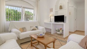 A living room with a sofa, a TV on a stand, a table with a bowl, and a window with curtains. - Holiday Home 'Chalet Fuente2 Shared Pool Family' with Shared Pool and Air Conditioning (Conil de la Frontera)