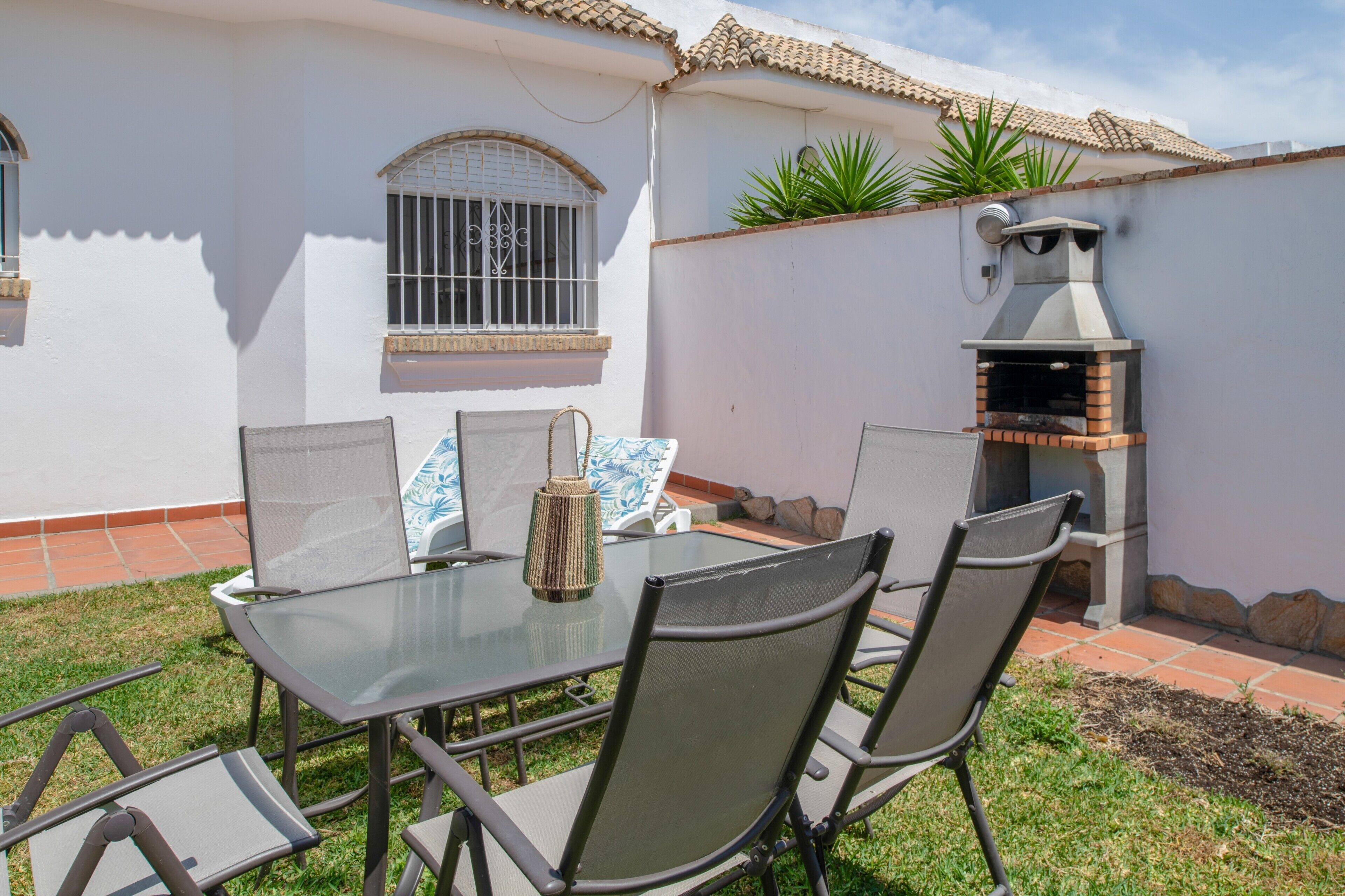 A patio with a glass table and chairs, a brick oven, and a window with bars.