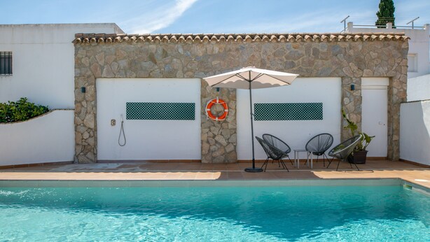 A pool area with stone walls, two doors, a lifebuoy, and two chairs. - Holiday Home 'Chalet Fuente2 Shared Pool Family' with Shared Pool and Air Conditioning (Conil de la Frontera)