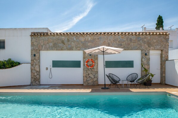 A pool area with stone walls, two doors, a lifebuoy, and two chairs.