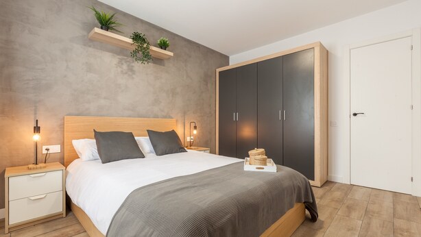 Un dormitorio moderno con una cama de madera, mesitas de noche, un armario y una estantería con plantas.