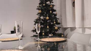 Una mesa de comedor con dos vasos transparentes, un posavasos tejido y un árbol de Navidad con adornos dorados.