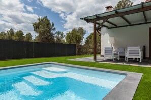 Une piscine avec un espace patio, un coin salon couvert et une vue sur les arbres.