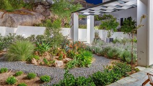 En moderne udendørs have med pergola, diverse planter og en grussti.