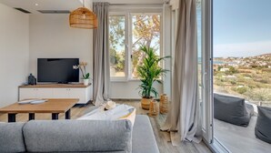 En moderne stue med tv, sofa, spisebord og store vinduer med udsigt over landskabet.