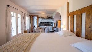 A bedroom with a large bed, a wooden headboard, a dining area with a table and chairs, and a kitchen visible through an archway. - Apartment "La maison de Constance" with Sea View, Terraces and Wi-Fi (Cavalaire-sur-Mer)