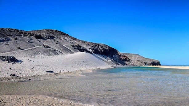 A beach with clear water, a sandy shore, and rocky cliffs.