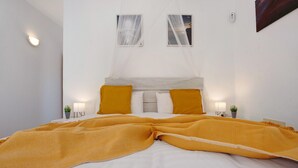 A bed with a white and yellow bedspread, two bedside tables with lamps, and a wall-mounted light fixture.