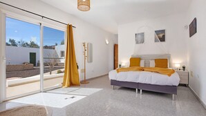 A bedroom with a bed, a bedside table, a nightstand, a window with curtains, and a view of the outside.