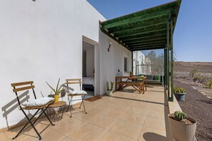 Un espace extérieur aménagé en patio, avec un coin salon abrité, une table et des plantes en pot.