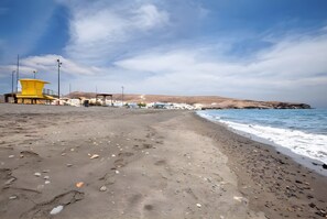 A beach with a lifeguard tower, a sandy shore, and a distant mountain. - Vacation Home "La Finca Las Estrellas" with Mountain View, Garden & Wi-Fi (Tarajalejo)