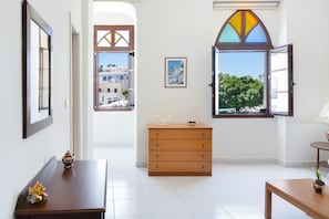 Una stanza con un comò di legno, un tavolo, una finestra con persiana aperta e un quadro appeso al muro.