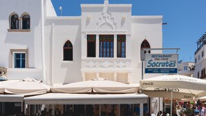 Een wit gebouw met een bord waarop 'Restaurant Socrates' staat, en terrasplekken met parasols.