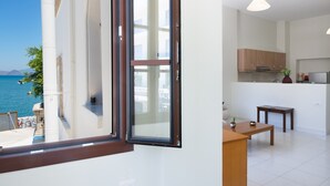 Een moderne keuken met houten kastjes, een eethoek met een tafel en stoelen, en uitzicht op zee door een raam.