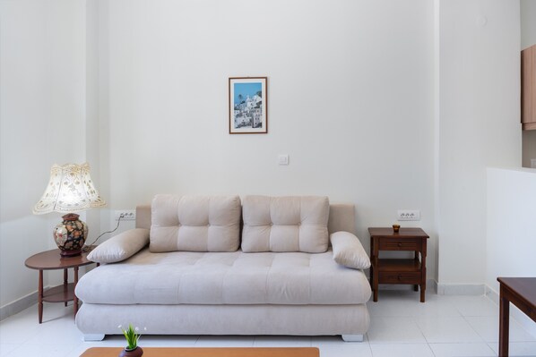 Un sofá de tonos neutros, una mesita de madera, una lámpara y un cuadro en la pared.