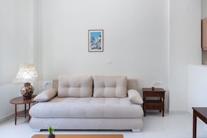 Un divano dai toni neutri, un piccolo tavolino in legno, una lampada e un quadro appeso al muro.